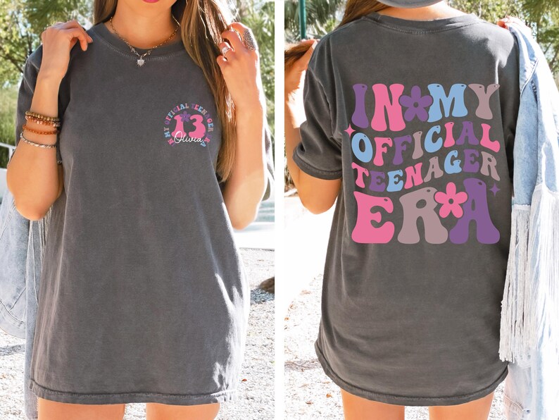 May include: A gray t-shirt with the text "In My Official Teenager Era" printed on the back in a retro font with pink, purple, and blue colors. The text is surrounded by flowers.