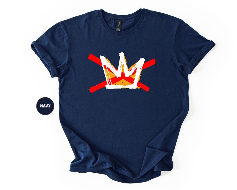 May include: Navy blue t-shirt featuring a graphic crown design in white, orange, and yellow, crossed by two red lines. The shirt has short sleeves and a crew neck. The word "NAVY" is in a navy circle.