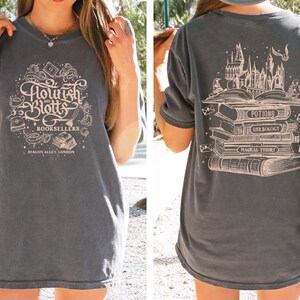 May include: A gray t-shirt with a vintage-style graphic of a bookstore called "Flourish and Blotts" with the text "Booksellers, Diagon Alley, London". The back of the shirt features a graphic of a stack of books with the titles "Potions", "Herbology", and "Magical Theory" and a castle in the background.