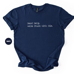Pu&ograve; includere: T-shirt blu navy con la scritta bianca "Send Help. We're Stuck With Him." La maglietta ha maniche corte e girocollo. Un cerchio blu navy con la scritta "NAVY" si trova nell'angolo in basso a sinistra.