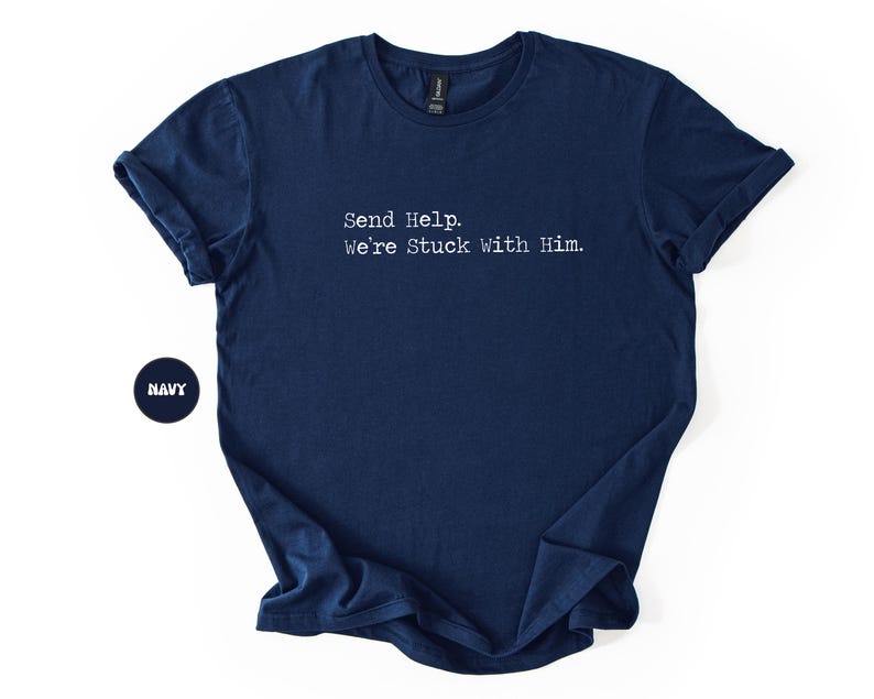Pu&ograve; includere: T-shirt blu navy con la scritta bianca "Send Help. We're Stuck With Him." La maglietta ha maniche corte e girocollo. Un cerchio blu navy con la scritta "NAVY" si trova nell'angolo in basso a sinistra.