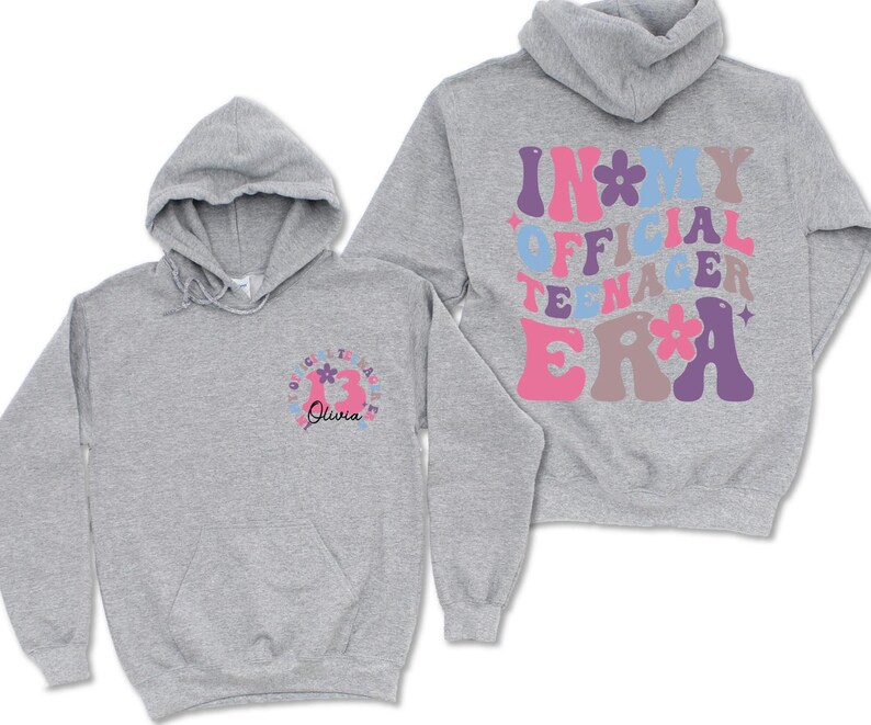 May include: Gray hooded sweatshirt with the text "In My Official Teenager Era" in colorful retro lettering on the back and a flower design on the front.