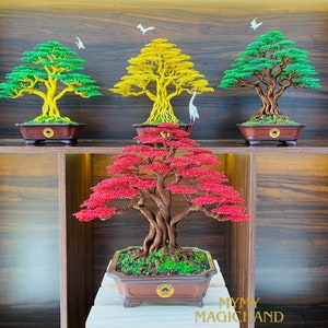 May include: A collection of handcrafted bonsai trees with vibrant foliage in green, yellow, and red. Each tree is meticulously detailed, set in a brown rectangular pot, and adorned with decorative birds. The trees are displayed on wooden shelves.