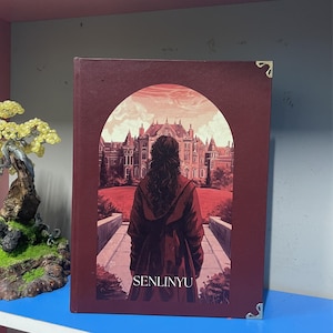 May include: A hardcover book with a burgundy cover featuring an illustration of a person in a red coat facing a large building. The book has gold corner protectors and the word "SENLINYU" is printed at the bottom.