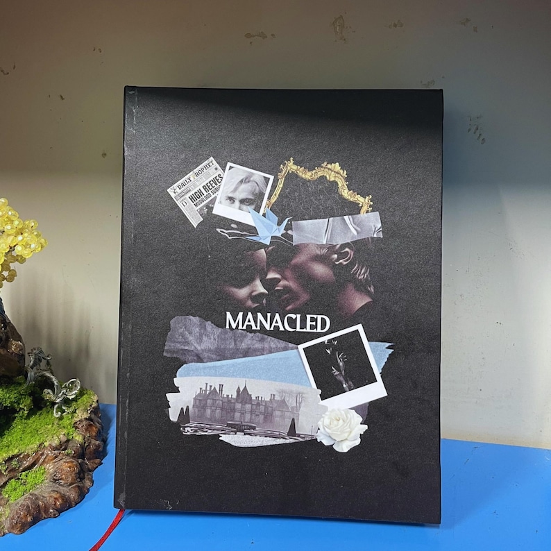 May include: A black book cover with the word "MANACLED" in white. The cover features a collage of images, including a newspaper clipping, a photo of a person, and a white rose.