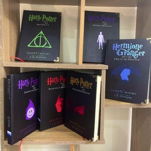 Puede incluir: Una estantería con diez libros de tapa dura negros con ilustraciones coloridas en las portadas. Los libros son todos parte de la serie de Harry Potter y tienen títulos como "Harry Potter y el Último Enemigo", "Harry Potter y las Sombras Mortales", "Hermione Granger y la Llamada del Fénix", "Harry Potter y la Legión del Caos", "Harry Potter y los Métodos de las Ratas" y "Harry Potter y la Piedra Filosofal".