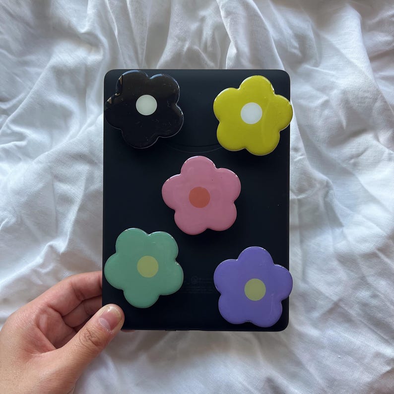 Peut inclure: Cinq poign&eacute;es de t&eacute;l&eacute;phone en forme de fleur color&eacute;es sur un fond noir. Les poign&eacute;es sont noires, jaunes, roses, vertes et violettes.