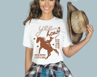May include: White t-shirt with a brown graphic of a woman riding a horse with the text "Yee Haw" and "Howdy" and "Forties" on it.
