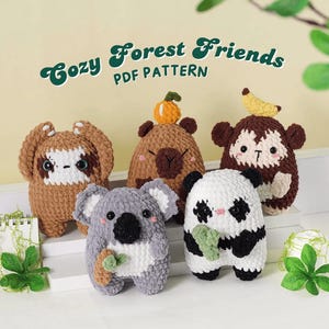 Könnte beinhalten: Fünf gehäkelte Waldtier-Plüschtiere: ein Faultier, ein Bär mit einem Kürbis, ein Affe mit einer Banane, ein Koala und ein Panda. Der Text "Cozy Forest Friends PDF Pattern" ist über den Plüschtieren zu sehen.