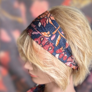 May include: A blue headband with a floral pattern in shades of red, orange, and white. The headband is made of fabric and has a simple design.