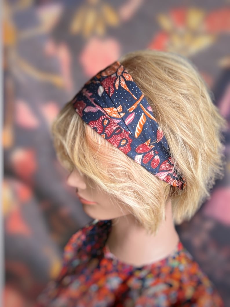 May include: A blue headband with a floral pattern in shades of red, orange, and white. The headband is made of fabric and has a simple design.