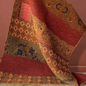 Peut inclure: Une couverture en tissu rouge, orange et marron à motifs géométriques. La couverture est pliée et drapée sur une surface.