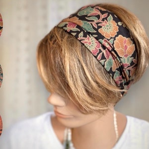 Può includere: Una fascia nera con un motivo floreale nei toni del pesca, rosa e verde. La fascia è indossata sulla testa di una persona, e il motivo floreale è visibile sul tessuto. Un accessorio di moda.