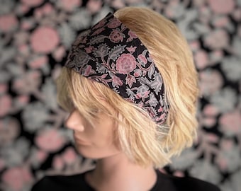 May include: A black headband with a pink and gray floral pattern. The headband is made of fabric and is worn on a person's head.