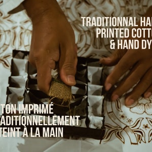 May include: Image of hands working with a hand-printed cotton textile. The text reads "TRADITIONNAL HAND PRINTED COTTON & HAND DYED" and "COTON IMPRIM&Eacute; TRADITIONNELLEMENT & TEINT &Agrave; LA MAIN". The textile has a brown floral pattern.