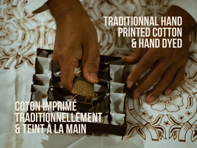 May include: Image of hands working with a hand-printed cotton textile. The text reads "TRADITIONNAL HAND PRINTED COTTON & HAND DYED" and "COTON IMPRIM&Eacute; TRADITIONNELLEMENT & TEINT &Agrave; LA MAIN". The textile has a brown floral pattern.