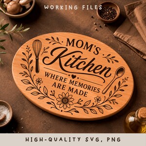 May include: An oval wooden chopping board featuring black laser-engraved text that reads MOM'S Kitchen WHERE MEMORIES ARE MADE. The design includes illustrations of a whisk, a spoon, and floral vine accents surrounding the central lettering.