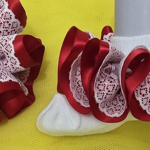 Könnte beinhalten: Weiße Socken mit roter Satin- und Spitzenausstattung. Die Socken haben ein Rüschendesign mit weißem Spitzeneinsatz und roter Satintrim. Auf gelbem Hintergrund.