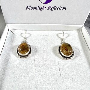 May include: A pair of silver earrings with brown and clear quartz stones. The earrings are in a white box with the text "Moonlight Reflection" on the lid.