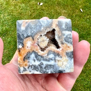 May include: A square-shaped, polished agate geode with a large, open cavity filled with white and brown crystals. The geode has a black, white, and brown banded pattern.