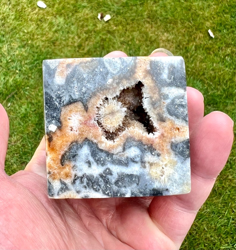 May include: A square-shaped, polished agate geode with a large, open cavity filled with white and brown crystals. The geode has a black, white, and brown banded pattern.