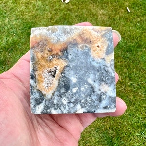 May include: A square, polished, grey, white, and brown agate stone with a natural, organic pattern. The stone has a rough, textured surface.