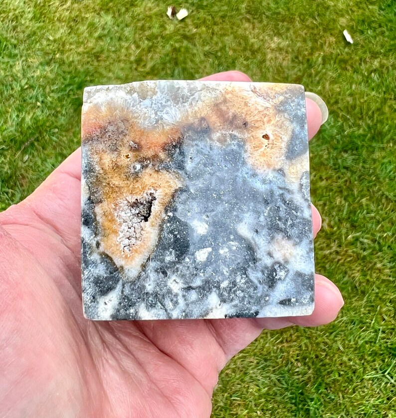 May include: A square, polished, grey, white, and brown agate stone with a natural, organic pattern. The stone has a rough, textured surface.