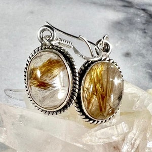 May include: Silver earrings with a gold rutilated quartz stone. The earrings have a rope-like design around the edge of the stone.