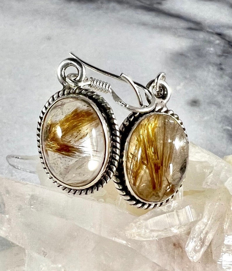 May include: Silver earrings with a gold rutilated quartz stone. The earrings have a rope-like design around the edge of the stone.