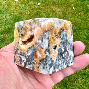 May include: A polished, multi-faceted, natural stone with a black, white, and yellow colour pattern. The stone has a rough, textured surface and a hollowed-out centre.