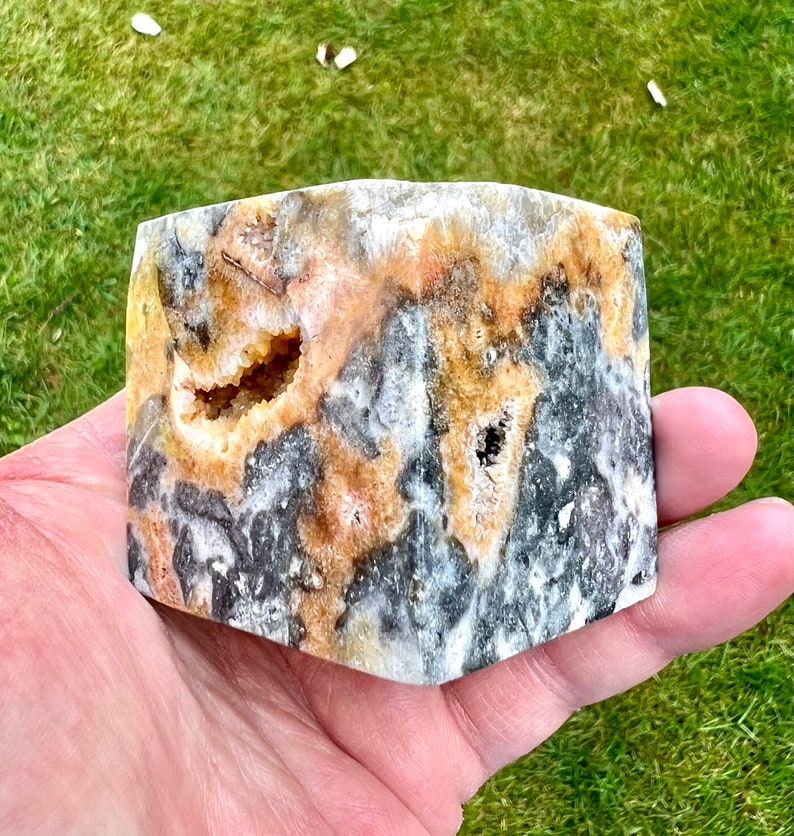 May include: A polished, multi-faceted, natural stone with a black, white, and yellow colour pattern. The stone has a rough, textured surface and a hollowed-out centre.