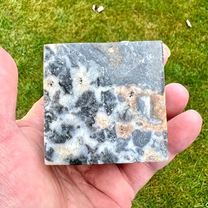 May include: A square piece of polished black, white and brown stone with a marbled pattern. The stone has a smooth, polished surface.