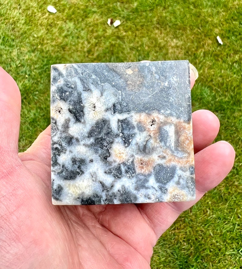 May include: A square piece of polished black, white and brown stone with a marbled pattern. The stone has a smooth, polished surface.