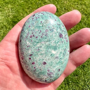 May include: A polished green and red gemstone with a smooth, oval shape. The stone has a speckled pattern of red and green.