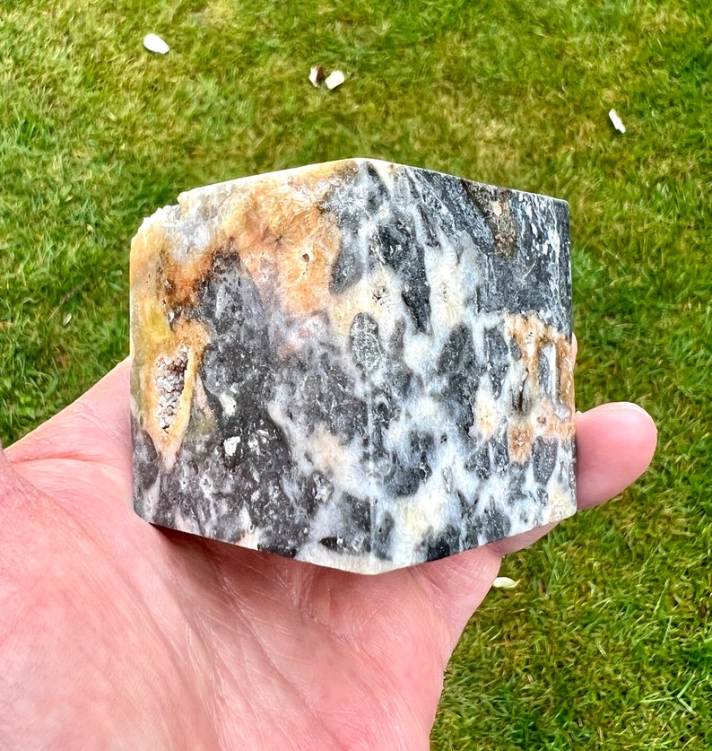 May include: A close-up of a black, white and yellow patterned stone. The stone has a rough, textured surface.