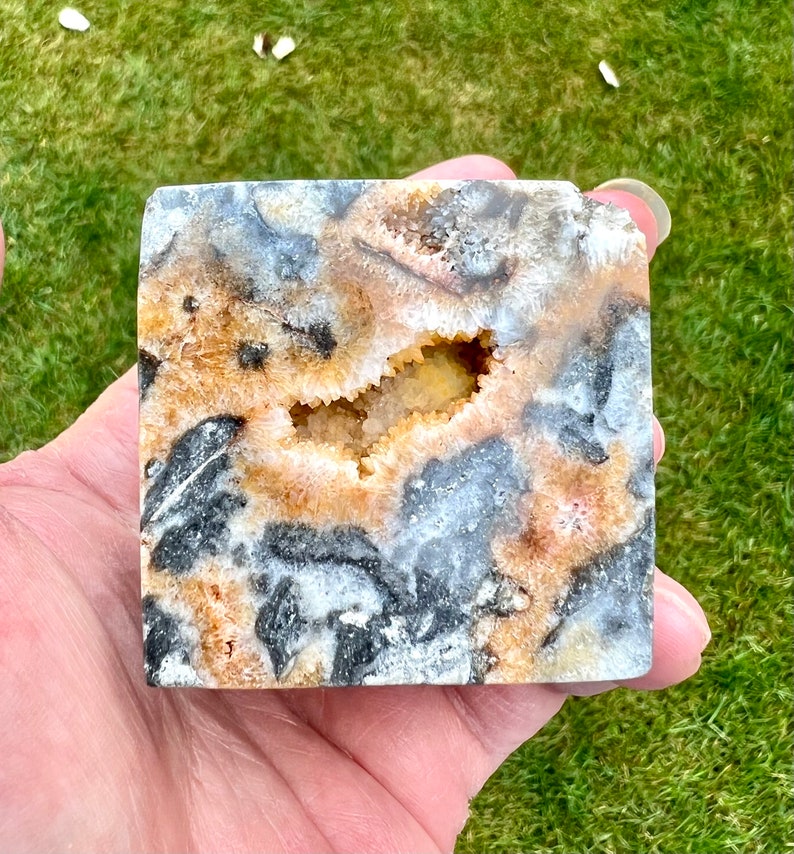 May include: A square-shaped agate geode with a natural opening revealing a crystal cave. The geode has a brown, white, and black colour pattern.