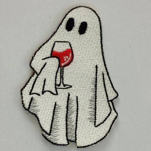 May include: White ghost with black eyes holding a red wine glass. The ghost is embroidered on a white fabric.