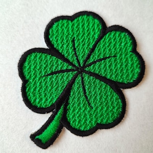 May include: A green four-leaf clover embroidered patch with black outlines.