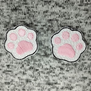 May include: Two white paw prints with pink outlines on a gray knitted fabric background.