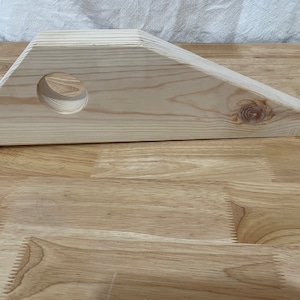 May include: A wooden triangular shelf with a round hole in the center. The shelf is made of light wood and has a natural finish.