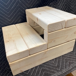 May include: A wooden two-step stool made of natural wood with a light brown finish.