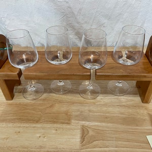 May include: Wooden wine glass holder with four clear wine glasses. The holder is shaped like a small bench with two arms on either side.