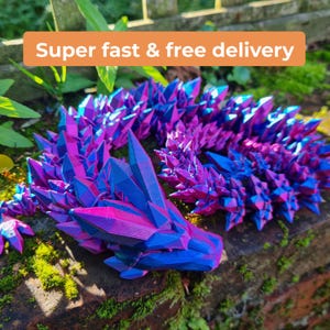 May include: A 3D printed crystal dragon sculpture with a blue and purple iridescent finish. The dragon is curled up in a sleeping position.