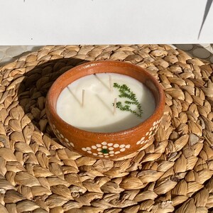 May include: A terracotta candle holder with white polka dots and a white candle inside. The candle has three wicks and a sprig of greenery on top.