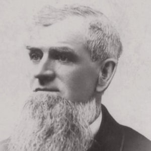 May include: Black and white portrait photograph of a man with a long white beard. He is wearing a dark suit jacket and has a serious expression.