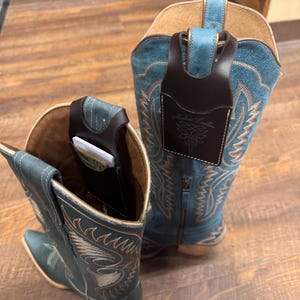 Puede incluir: Dos botas de vaquero turquesas con intrincadas costuras y detalles en cuero marrón. Cada bota tiene un bolsillo de cuero marrón adjunto en la parte superior, uno con tarjetas visibles. Los bolsillos están grabados con las palabras "Madsen Leather" y un diseño decorativo.