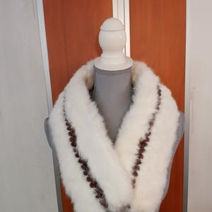 May include: White fur collar with brown trim. The collar is made of soft, fluffy fur and has a simple, elegant design.