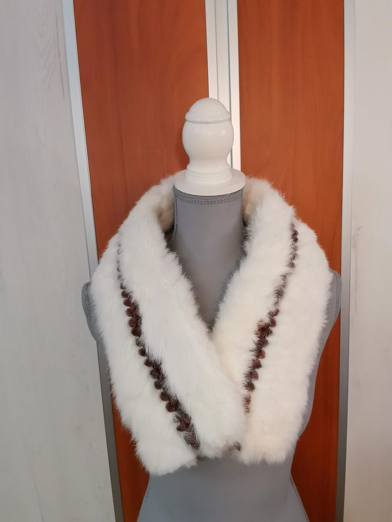 May include: White fur collar with brown trim. The collar is made of soft, fluffy fur and has a simple, elegant design.