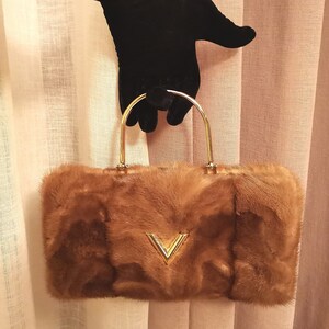 May include: A brown fur handbag with a gold top handle and a gold V-shaped design on the front.