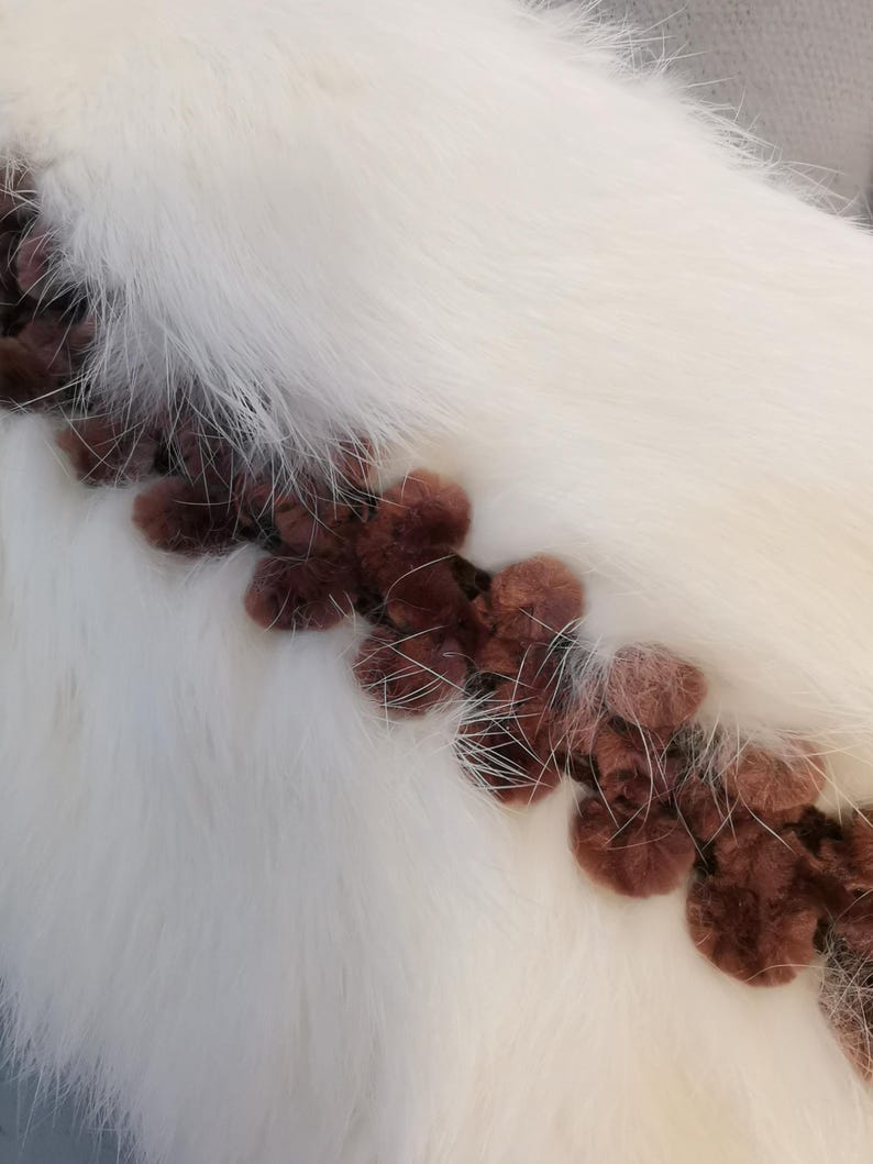 May include: White faux fur fabric with a brown trim of fluffy pom-poms.